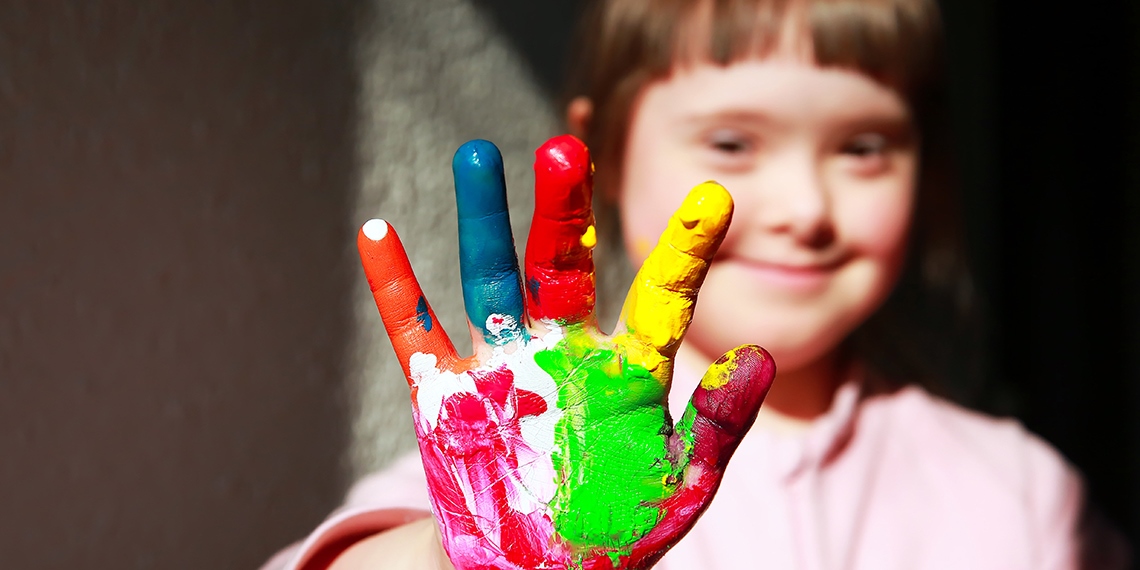 A smiling girl holding up a hand covered in bright paint